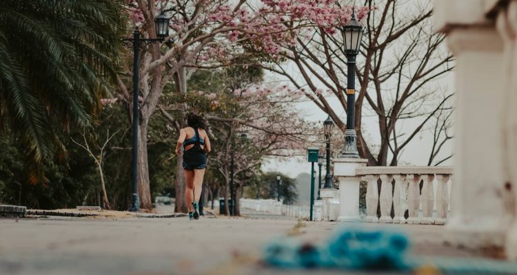 A woman jogs through a picturesque park lined with blooming spring trees and vintage lamps.